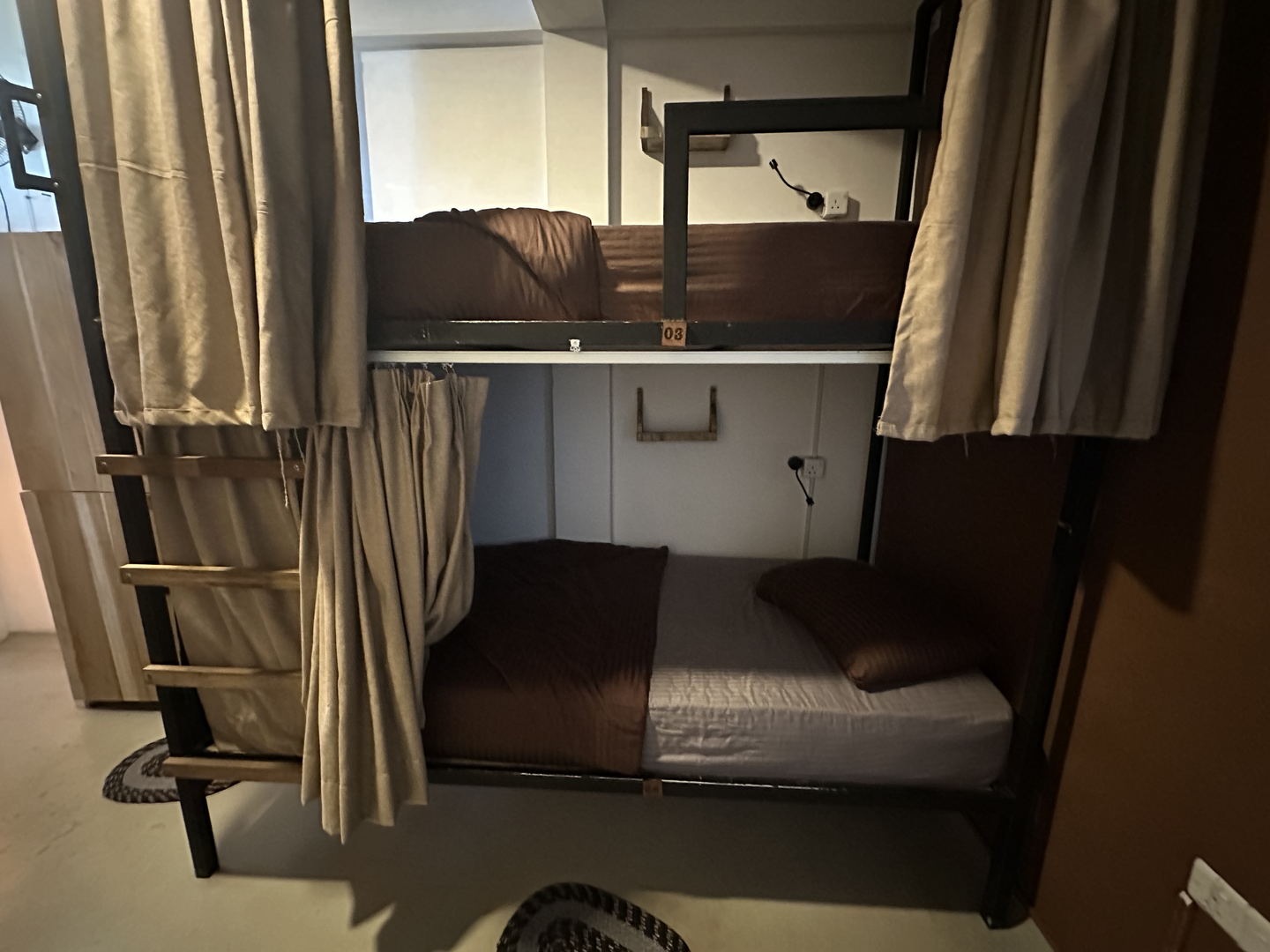 A bunk in one of the dormitories: a steel frame, a made bed and a full-length curtain that pulls across the opening.