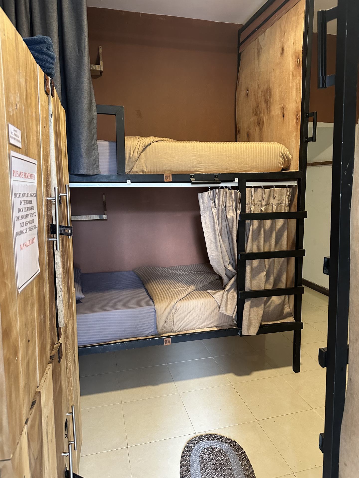 Beds one and two in a four-bed mixed dorm, seen past an open locker door: a curtained lower bunk and the bunk above it.