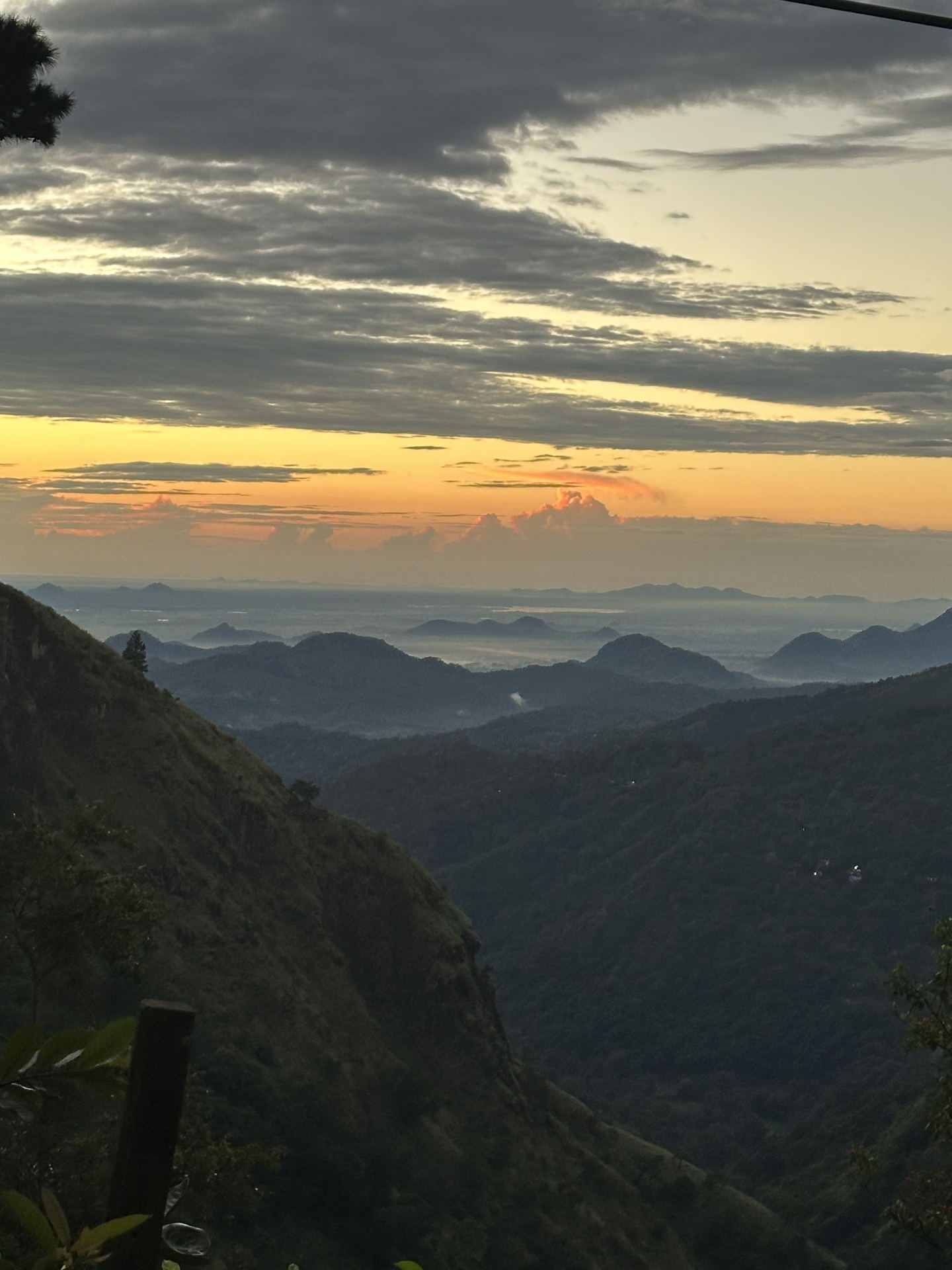 The gap at the end of the day: a dark hillside falling away to ranges of hills in haze, under a band of orange cloud.